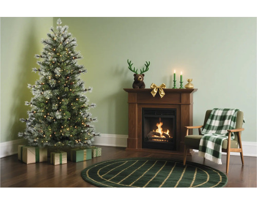 Sfeervol ingerichte woonkamer met verlichte kunstkerstboom, haard, fauteuil met geruite deken en kerstversiering.