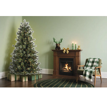 Kerstachtig ingerichte woonkamer met een kunstmatige besneeuwde kerstboom met lichtjes naast een houten haard en een fauteuil.