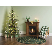 Feestelijke woonkamer met een verlichte kerstboom, houten haard, groen vloerkleed en fauteuil met geruite deken.