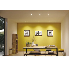 Een modern ingerichte kamer met gele muurverf, ronde plafondinbouwspots en een massief houten tafel met bankje.