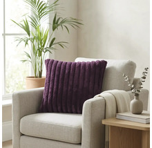 Paars geribbeld sierkussen op een lichtgrijze fauteuil in een lichte kamer met kamerplant en bijzettafel.