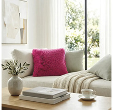Roze hoogpolig kussen op een lichte bank in een modern ingerichte, lichte woonkamer.