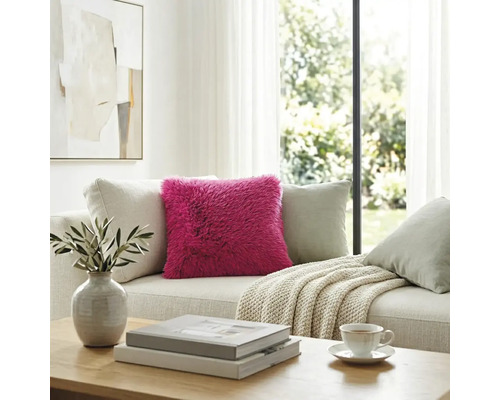 Roze hoogpolig kussen op een lichte bank in een modern ingerichte, lichte woonkamer.