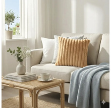 Lichte woonkamer met een lichte bank, een geribbeld okerkleurig kussen, diverse sierkussens, blauwe plaid en een rotan tafel.