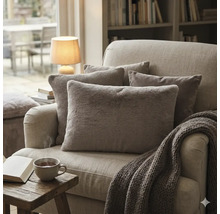 Gezellige fauteuil met diverse sierkussens van imitatiebont en breisel, plus een grofgebreid plaid in een lichte woonkamer.