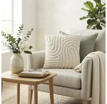 Lichte woonkamer met gestoffeerde fauteuil, sierkussen met textuur, wafelgebreide deken en houten bijzetafel met bloemenvaas.