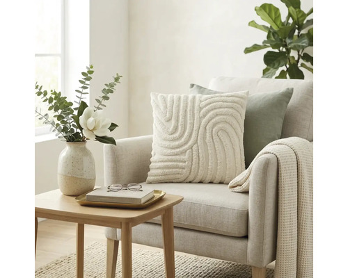 Lichte woonkamer met gestoffeerde fauteuil, sierkussen met textuur, wafelgebreide deken en houten bijzetafel met bloemenvaas.