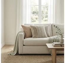 Lichte woonkamer met moderne stoffen bank, kussens met textuur en gebreide deken. Een jute vloerkleed en houten tafel vullen de ruimte aan.
