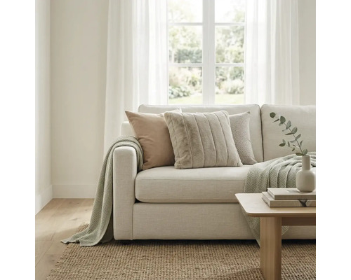 Lichte woonkamer met moderne stoffen bank, kussens met textuur en gebreide deken. Een jute vloerkleed en houten tafel vullen de ruimte aan.