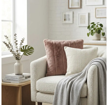 Lichte woonkamer met een witte bouclé fauteuil, een oudroze imitatiebont kussen, een wit sierkussen en een grijze plaid.