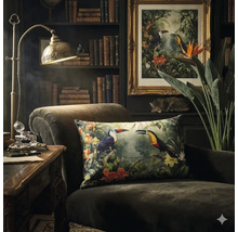 Donkere fauteuil met decoratief kussen met toekanmotief in een klassiek ingerichte kamer met boekenkast en messing bureaulamp.
