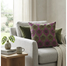 Sierkussen met paars en groen geometrisch patroon op een lichtgrijze fauteuil in een lichte woonkamer met kamerplant.