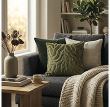 Moderne woonkamer met grijze bank, groene en beige sierkussens, gebreide deken en houten bijzettafel voor een licht raam.