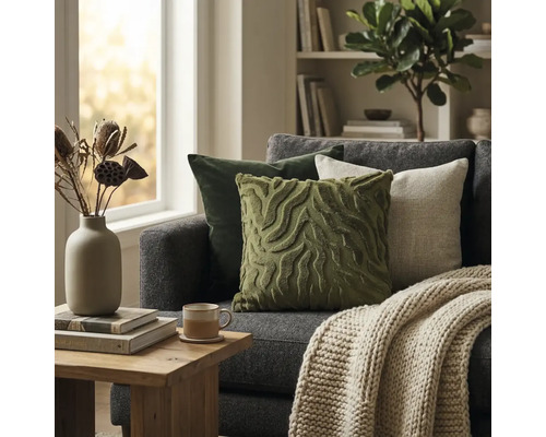 Moderne woonkamer met grijze bank, groene en beige sierkussens, gebreide deken en houten bijzettafel voor een licht raam.