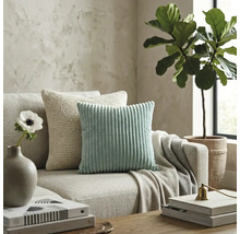 Moderne woonkamer met een mintgroen corduroy kussen en een beige gebreid kussen op een neutrale stoffen bank.