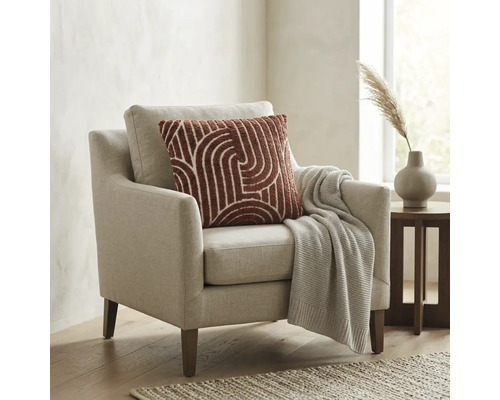Moderne fauteuil met lichte stoffen bekleding, sierkussen met patroon en gebreide deken in een lichte woonkamer.