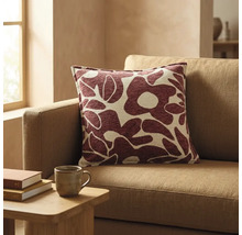Vierkant sierkussen met abstract bloemenpatroon in donkerrood en beige op een bank in een lichte woonkamer.