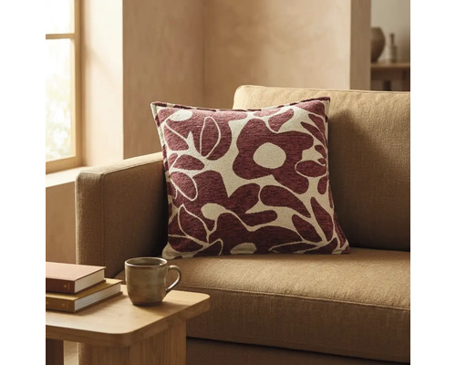 Vierkant sierkussen met abstract bloemenpatroon in donkerrood en beige op een bank in een lichte woonkamer.