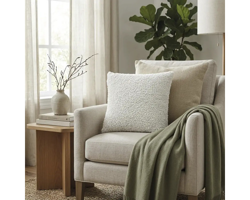 Lichte fauteuil met gestructureerd kussen en groene plaid in een lichte woonkamer naast een houten bijzettafel.