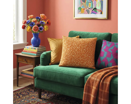 Groene fluwelen bank met luipaardprint kussen, een oranje deken, een bijzettafel met bloemen en ingelijste wandkunst.