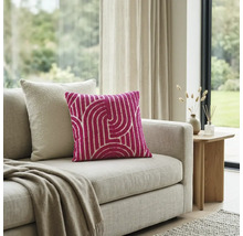 Roze sierkussen met wit geometrisch patroon op een beige bank in een lichte woonkamer.