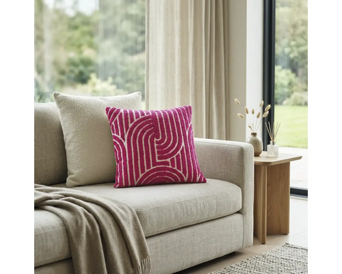 Roze sierkussen met wit geometrisch patroon op een beige bank in een lichte woonkamer.