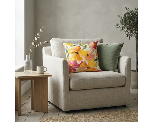 Sierkussen met kleurrijk bloemenpatroon op een lichte fauteuil in een lichte woonkamer naast een bijzettafel