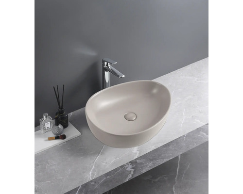 Ovale opzetwastafel in mat beige op een werkblad met marmerlook en een chromen kraan.