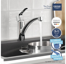 Keukenkraan in chroom bij een donkere spoelbak, water stroomt in een roestvrijstalen pan. GROHE Logo en montagesymbolen inbegrepen.