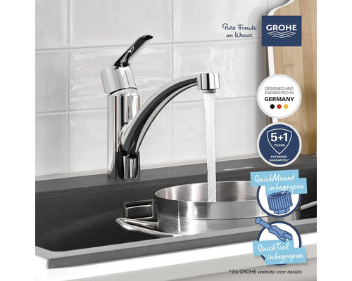 Keukenkraan in chroom bij een donkere spoelbak, water stroomt in een roestvrijstalen pan. GROHE Logo en montagesymbolen inbegrepen.