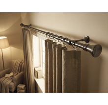 Metalen gordijnroede met ringen en stoffen gordijnen in een lichte kamer met raam en fauteuil.