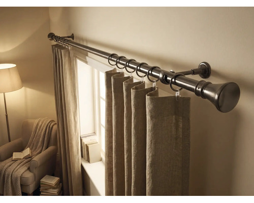 Metalen gordijnroede met ringen en stoffen gordijnen in een lichte kamer met raam en fauteuil.
