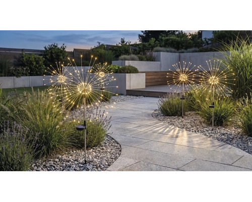 Solar tuinlampen in paardenbloem-ontwerp met lichtdiodes langs een bestraat pad in een modern ingerichte tuin tijdens de schemering.