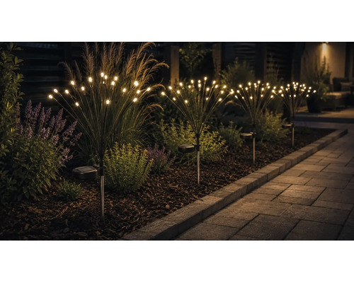 Tuinverlichting op zonne-energie in vuurwerkontwerp met warmwitte led-lampen in een plantenborder naast een bestraat tuinpad.