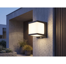Moderne vierkante LED-buitenwandlamp met bewegingssensor, verlicht op een gestructureerde muur bij een terras.