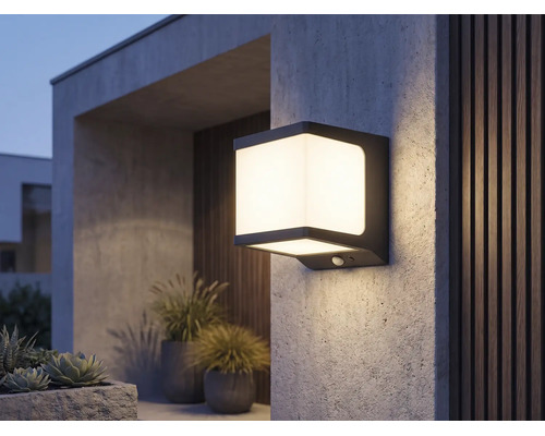 Moderne vierkante LED-buitenwandlamp met bewegingssensor, verlicht op een gestructureerde muur bij een terras.