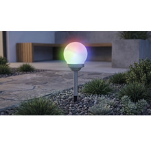 Tuinverlichting op zonne-energie in bolvorm met meerkleurige RGB-verlichting, op een grondpen in een grindbed met planten.