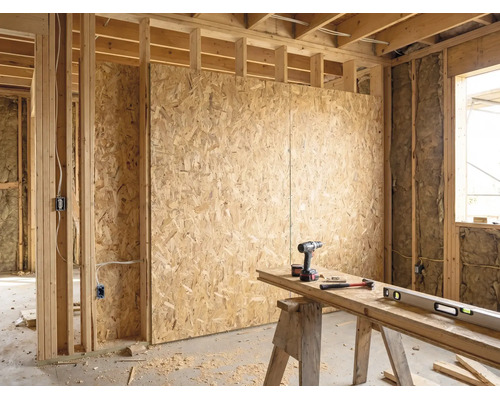 Lichte ruwbouw met OSB-platen op houten regelwerk, isolatie en een georganiseerde werkbank met boormachine, hamer en waterpas.