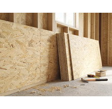 OSB-platen tegen een houten wand in een lichte ruwbouw met een hamer, meetlint en schroeven op de vloer.