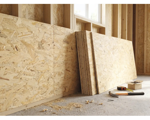 OSB-platen tegen een houten wand in een lichte ruwbouw met een hamer, meetlint en schroeven op de vloer.