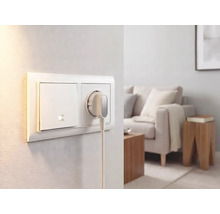 Lichtschakelaar en stopcontact met platte stekker aan een muur in een lichte, modern ingerichte woonkamer.