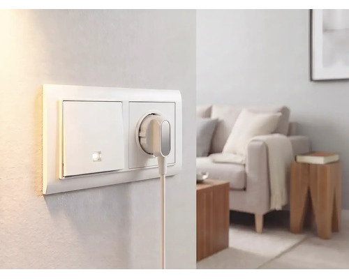 Lichtschakelaar en stopcontact met platte stekker aan een muur in een lichte, modern ingerichte woonkamer.