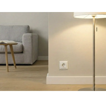 Moderne woonkamer met een wit stopcontact aan de muur, een vloerlamp, houten vloer en een grijze bank op de achtergrond.