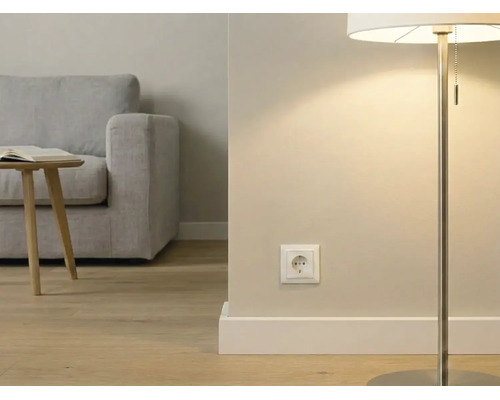 Moderne woonkamer met een wit stopcontact aan de muur, een vloerlamp, houten vloer en een grijze bank op de achtergrond.