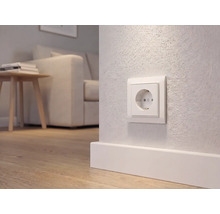Wit stopcontact met randaarde op een wand boven een plint in een modern ingerichte woonkamer met houten vloer.