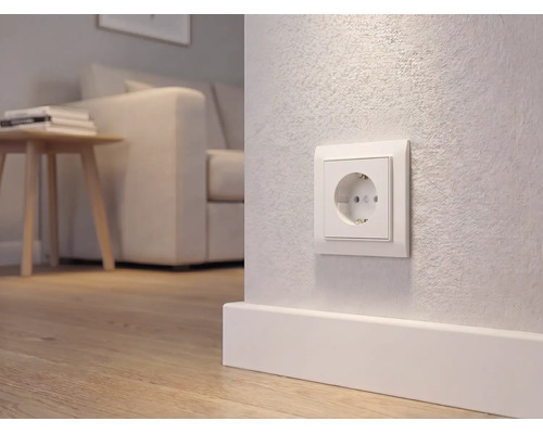 Wit stopcontact met randaarde op een wand boven een plint in een modern ingerichte woonkamer met houten vloer.