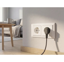 Dubbel stopcontact op een lichte muur in een moderne woonkamer met een stekker en omvlochten kabel.