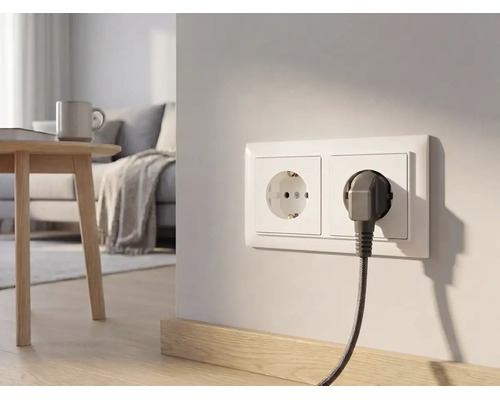 Dubbel stopcontact op een lichte muur in een moderne woonkamer met een stekker en omvlochten kabel.
