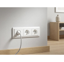 Drievoudig stopcontact met een aangesloten kabel op een witte muur boven een houten plint in een moderne kamer.