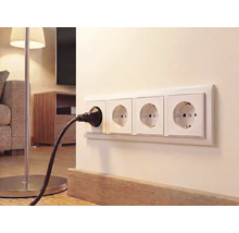 4-voudige wandcontactdoos aan een lichte wand in de woonkamer met een zwarte stekker van een vloerlamp.